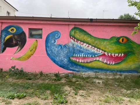 Un muro rosa dipinto con un coccodrillo verde, un tucano e una banana.