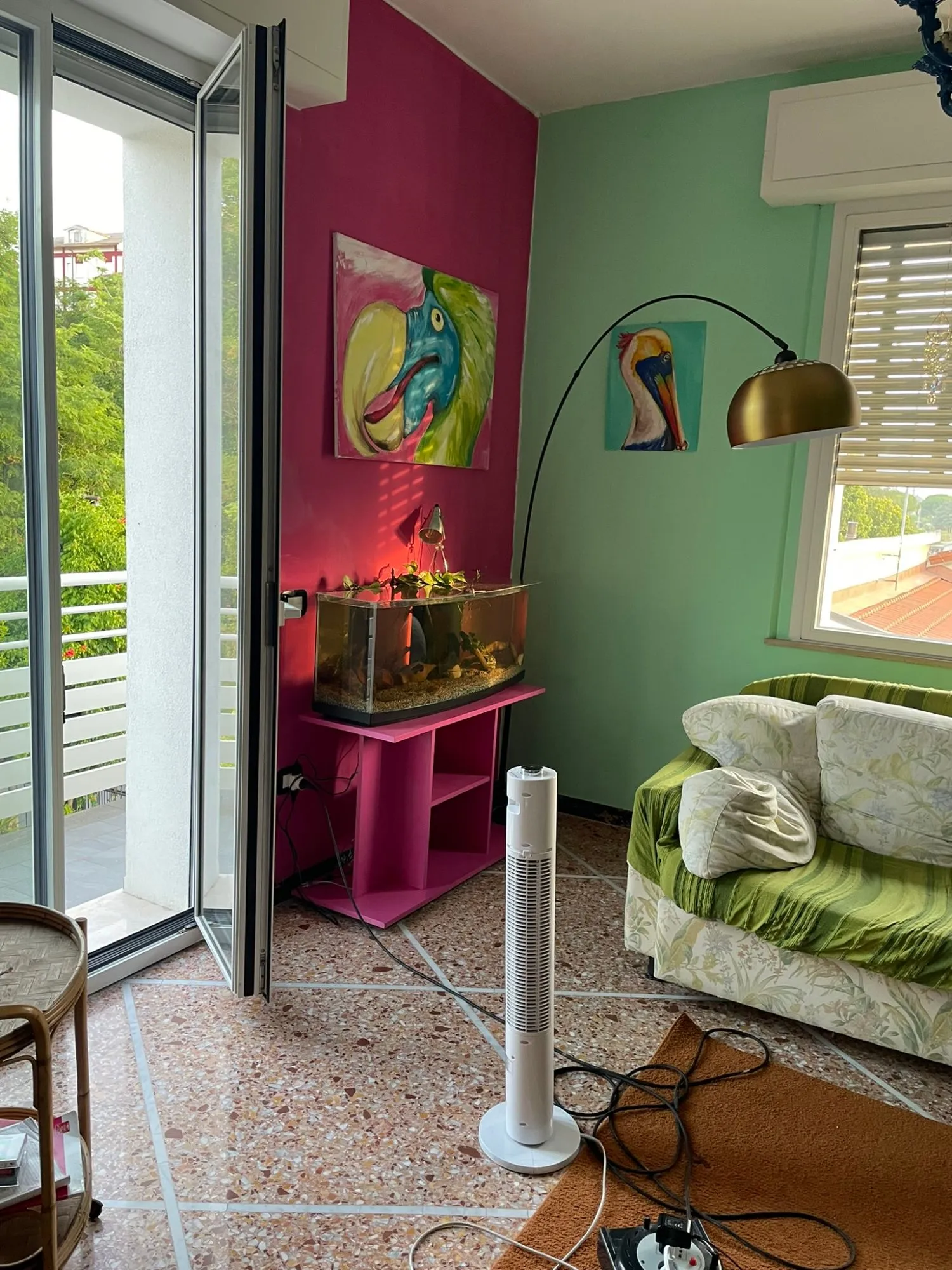 Salotto con una parete fucsia, una verde menta, quadri di pappagalli, un acquario e una lampada ad arco d'ottone.